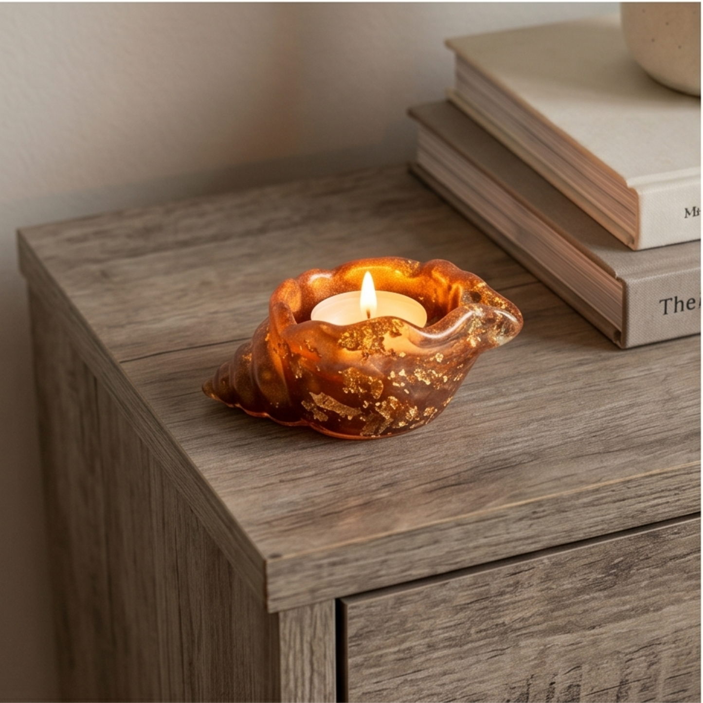 Suporte decorativo em forma de búzio em resina caramelo com flocos dourados e vela acesa sobre mesa de madeira