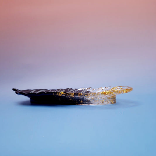 Bandeja decorativa em resina epóxi em forma de pena, acabamento preto com folhas douradas, vista lateral minimalista.”