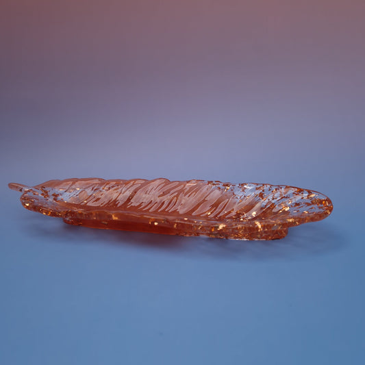 Bandeja decorativa em resina epóxi em formato de pena, acabamento cobre com detalhes dourados, vista lateral sobre fundo azul.
