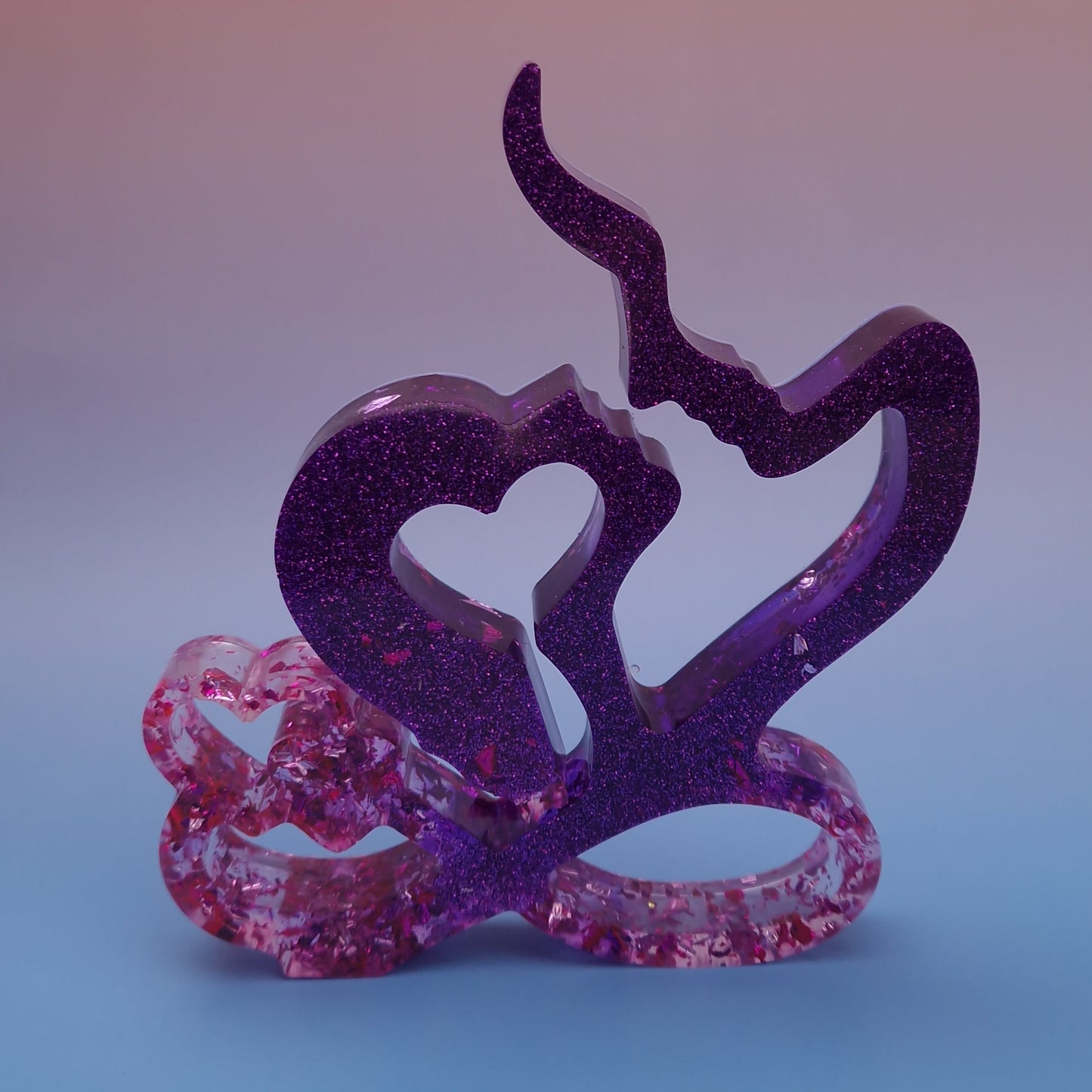 Escultura decorativa em resina epóxi representando casal com coração, em tons de roxo com brilho e detalhes em folhas de ouro rosa, peça artesanal contemporânea.