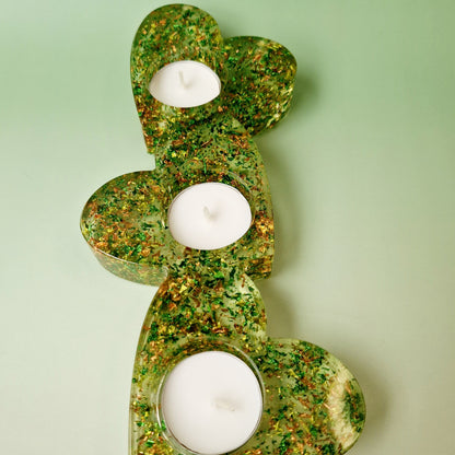 Castiçal triplo em formato de coração em resina epóxi verde translúcida, com três porta-velas e folhas metálicas douradas, vista superior.