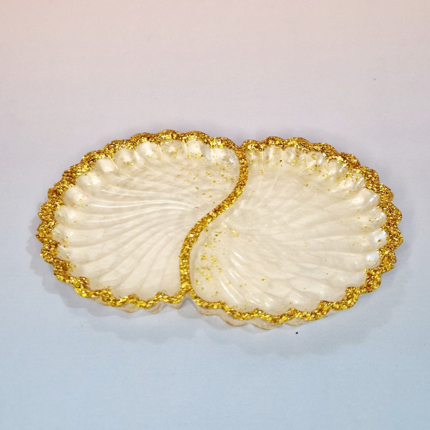 Taça decorativa Twin Shells em resina clara, com formato de conchas duplas, acabamento perolado e bordas com efeito dourado texturizado, vista superior.