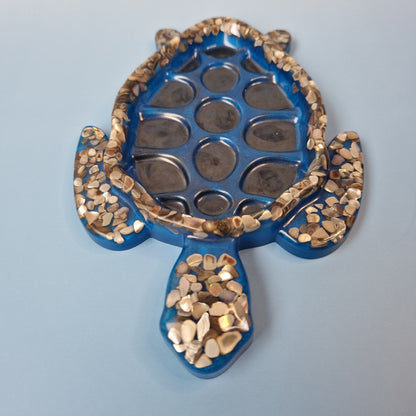 Tartaruga decorativa artesanal em resina epóxi azul com detalhes de conchas, vista frontal sobre fundo claro.