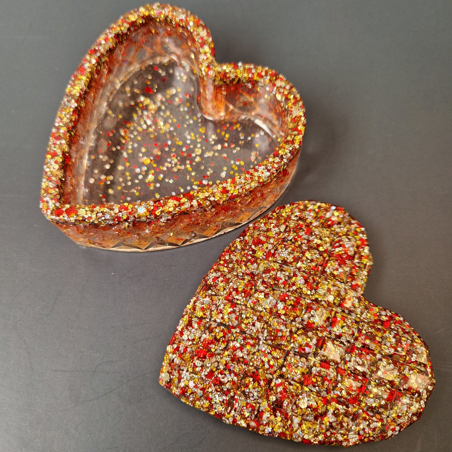 Caixa decorativa coração em resina epóxi aberta, interior transparente com detalhes em glitter vermelho e dourado.