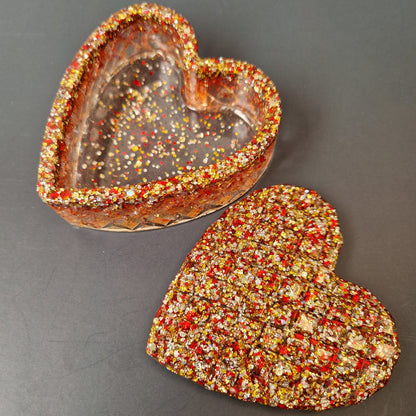 Caixa decorativa coração em resina epóxi aberta, interior transparente com detalhes em glitter vermelho e dourado.