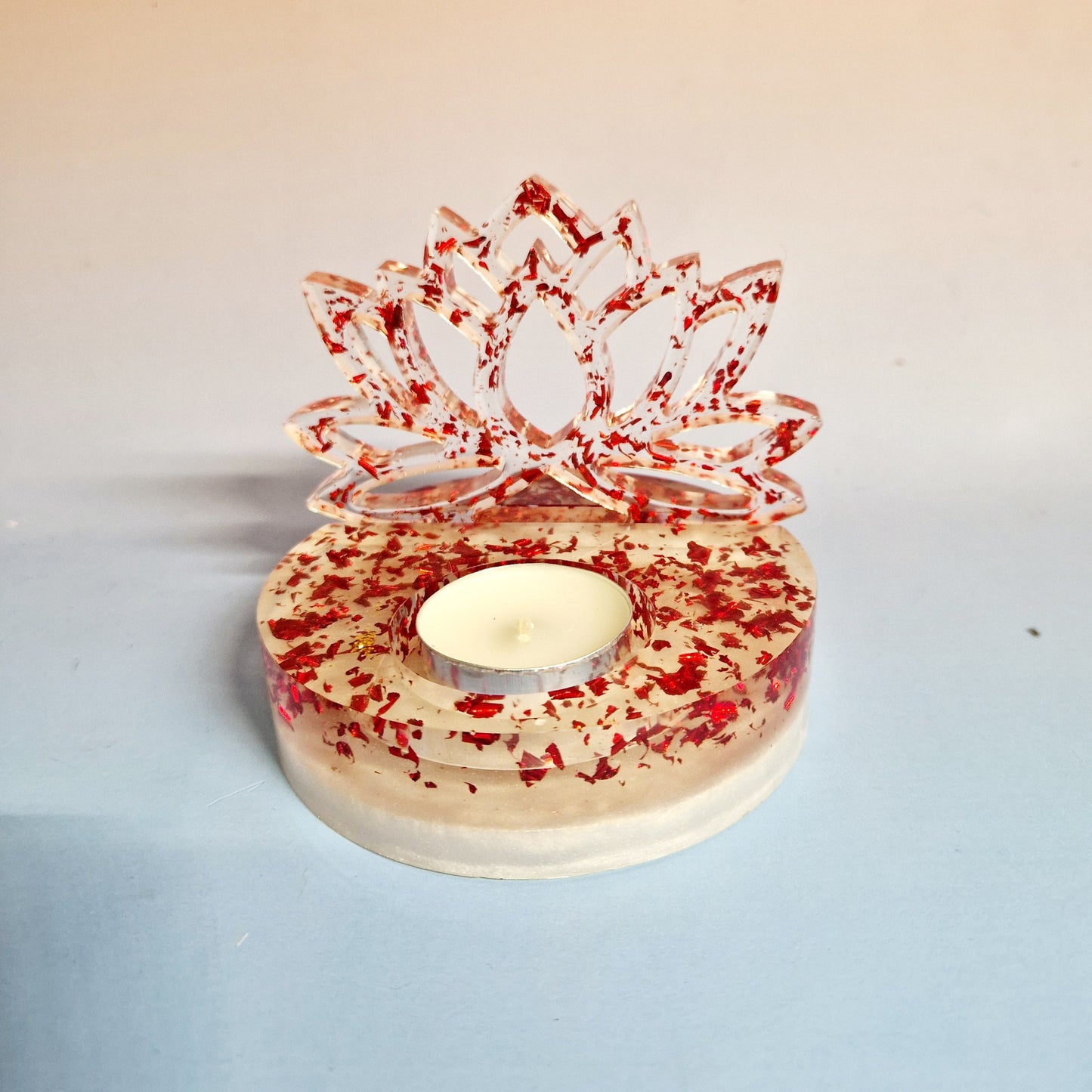 Suporte de vela tealight em resina de alta transparência com a silhueta vertical de uma Flor de Lótus. A base e a flor são preenchidas com flocos metálicos vermelhos vibrantes, com uma vela de cera inserida no encaixe central