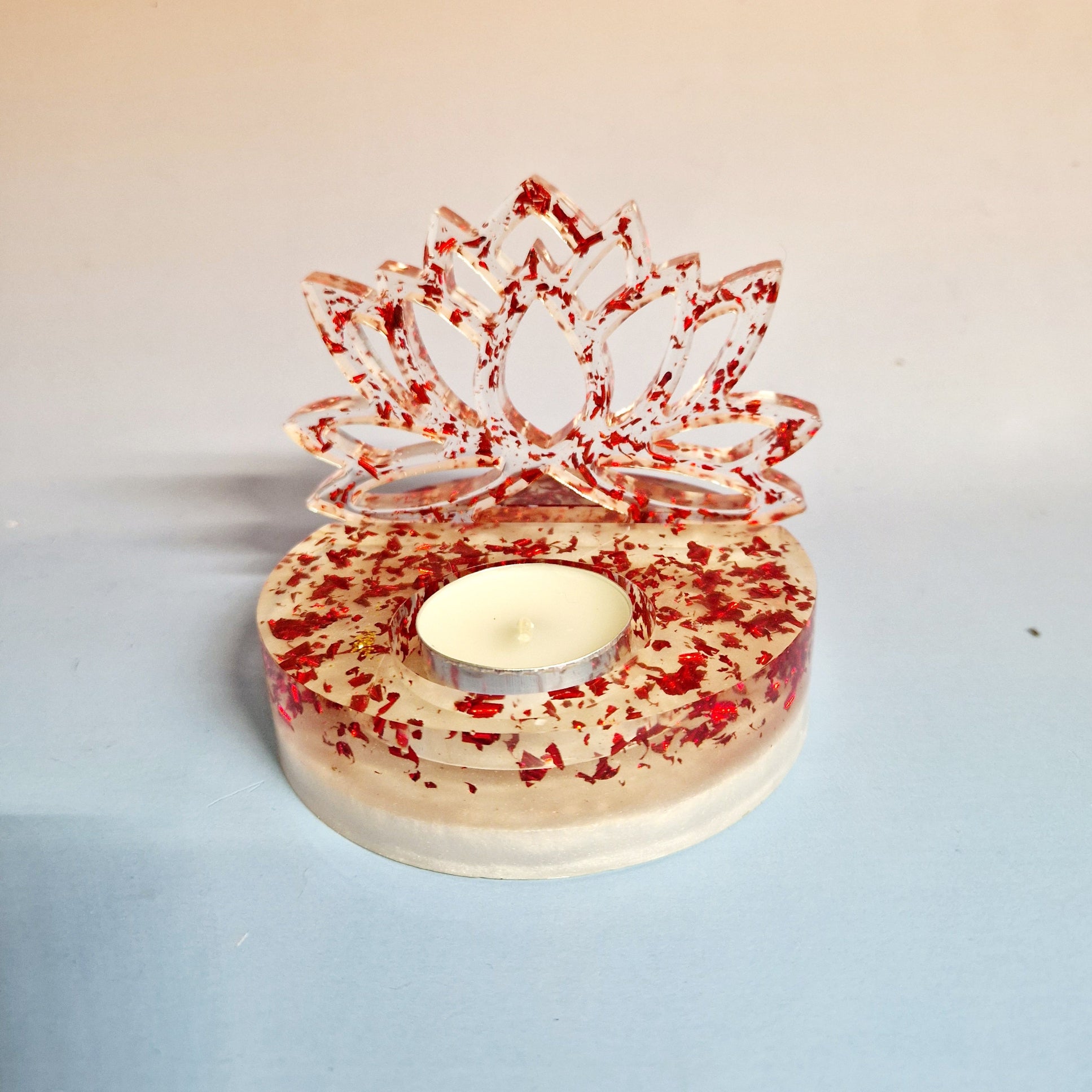 Suporte de vela tealight em resina de alta transparência com a silhueta vertical de uma Flor de Lótus. A base e a flor são preenchidas com flocos metálicos vermelhos vibrantes, com uma vela de cera inserida no encaixe central