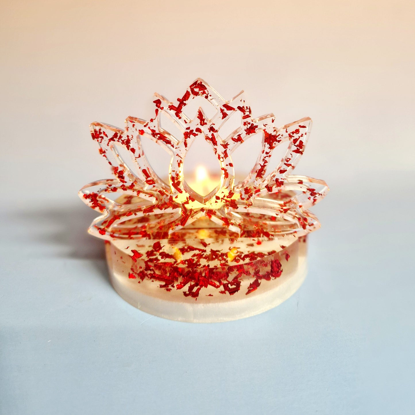 Suporte de vela tealight em resina de alta transparência com a silhueta vertical de uma Flor de Lótus. A base e a flor são preenchidas com flocos metálicos vermelhos vibrantes, com uma vela de cera  inserida no encaixe central