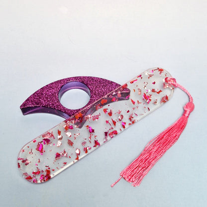 Marcador de página artesanal em resina transparente com folhas rosa metálicas, acessório curvo roxo com glitter e pingente de tassel rosa.