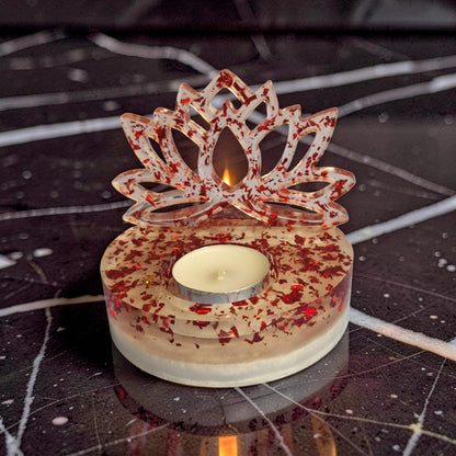 Porta-vela Flor de Lótus artesanal em resina com vela acesa sobre superfície de mármore preto.