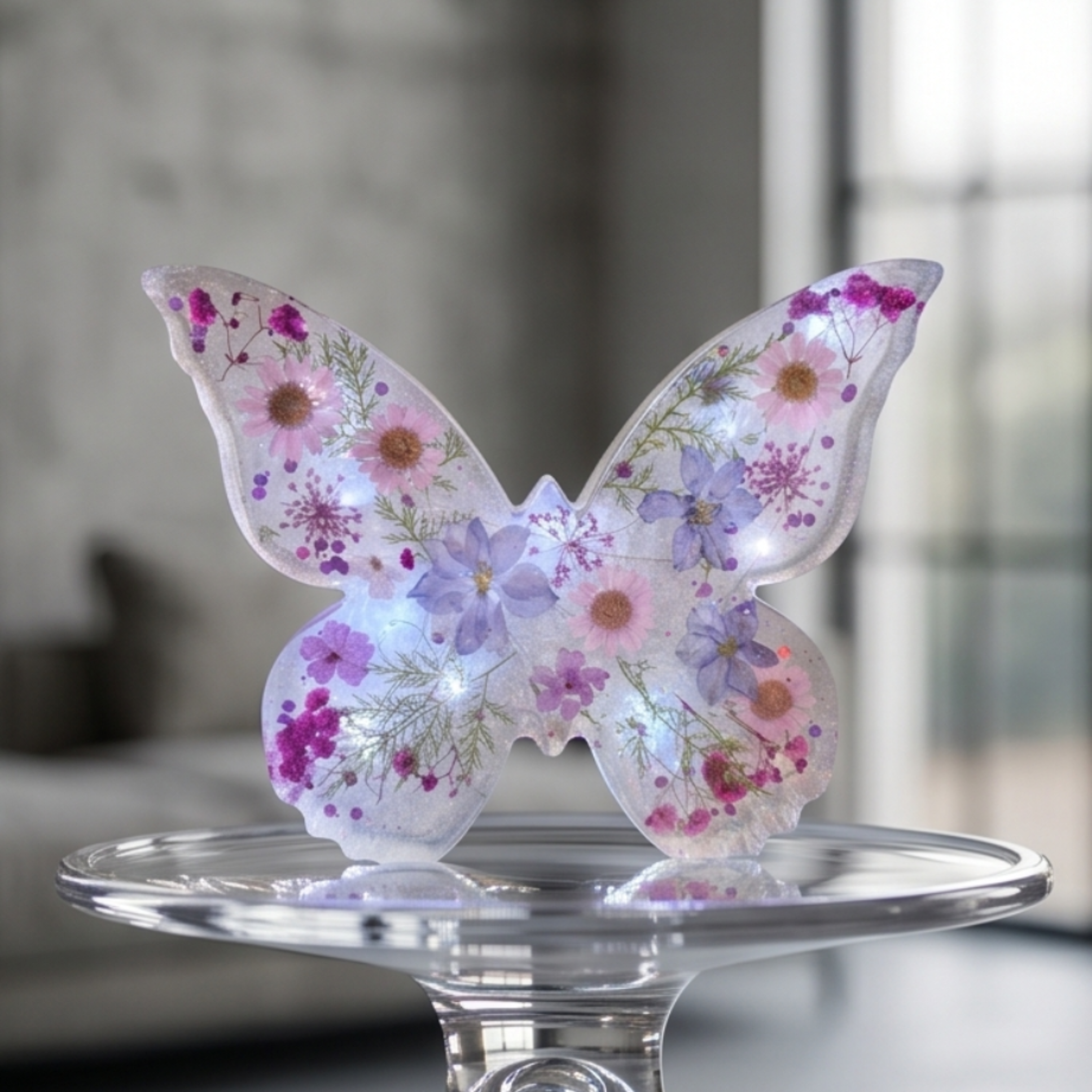 Detalhe da Borboleta Alice com iluminação LED, revelando as flores naturais e os reflexos iridescentes da resina artesanal.