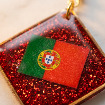 Pormenor dos brincos artesanais com Bandeira de Portugal em resina epóxi vermelha, acabamento brilhante e detalhes dourados.