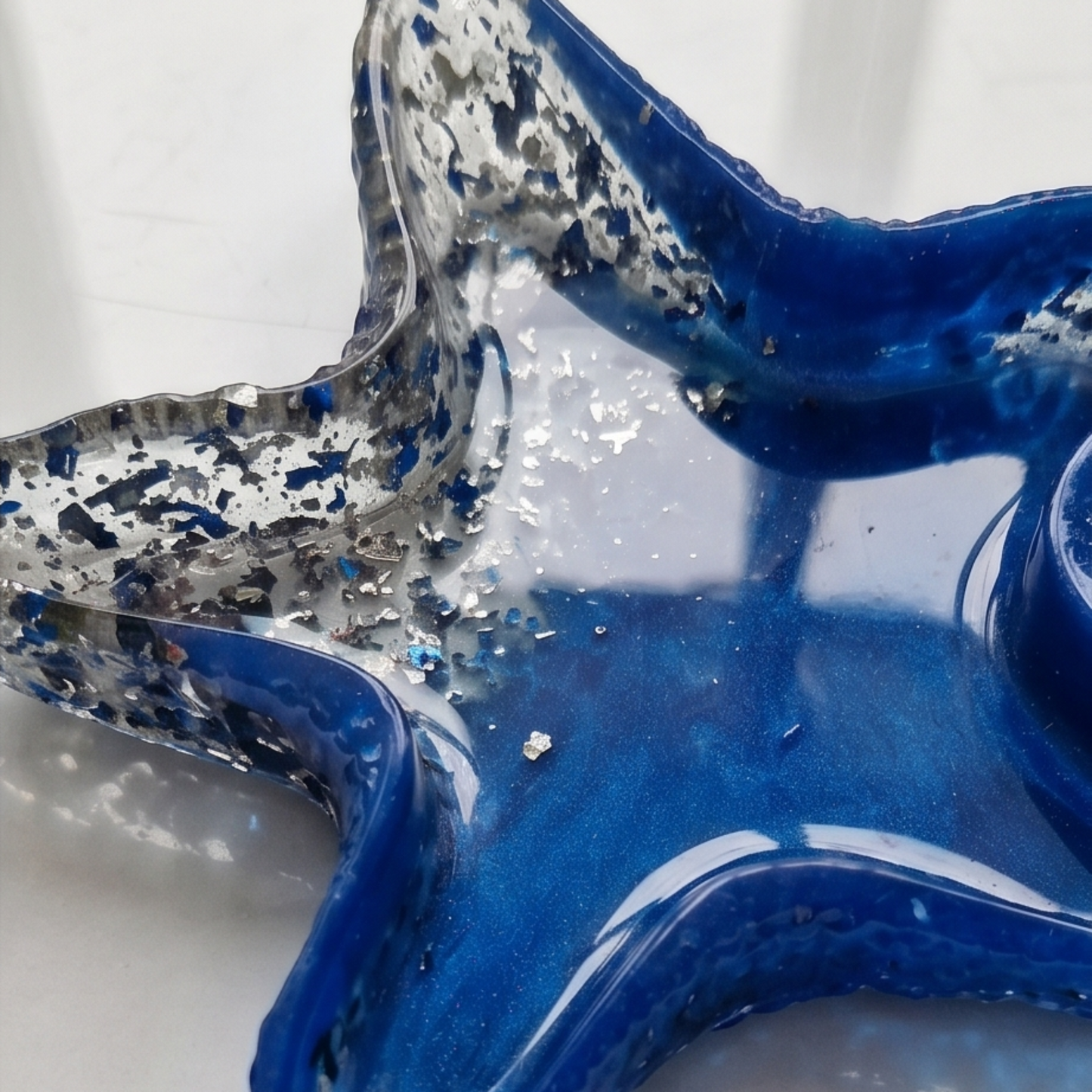 Detalhe de peça em forma de estrela-do-mar em resina azul com efeito metálico e acabamento brilhante