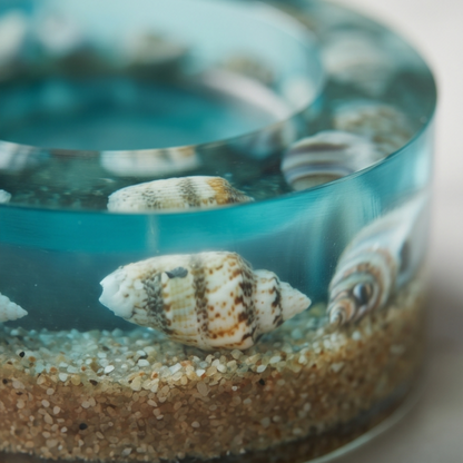 Detalhe de suporte para velas tealight em resina transparente com conchas naturais e areia, inspirado no fundo do mar