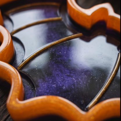 Pormenor do acabamento brilhante do tabuleiro morcego em resina epóxi, destacando os tons roxo e preto, os contornos laranja e os detalhes dourados.